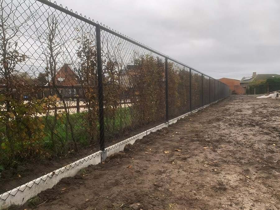 Hoge zwarte draadomheining met betonnen kantplaat langs een perceel, geplaatst door Lamon Hekwerk